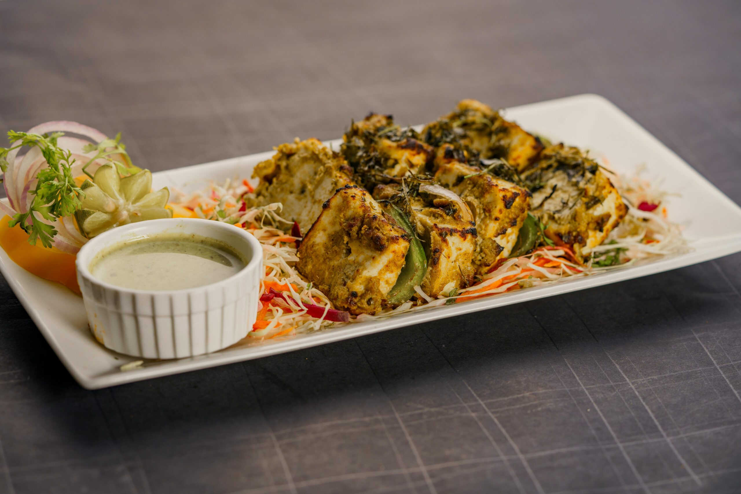 Succulent herb-crusted paneer tikka served with chutney and salad on a stylish plate.